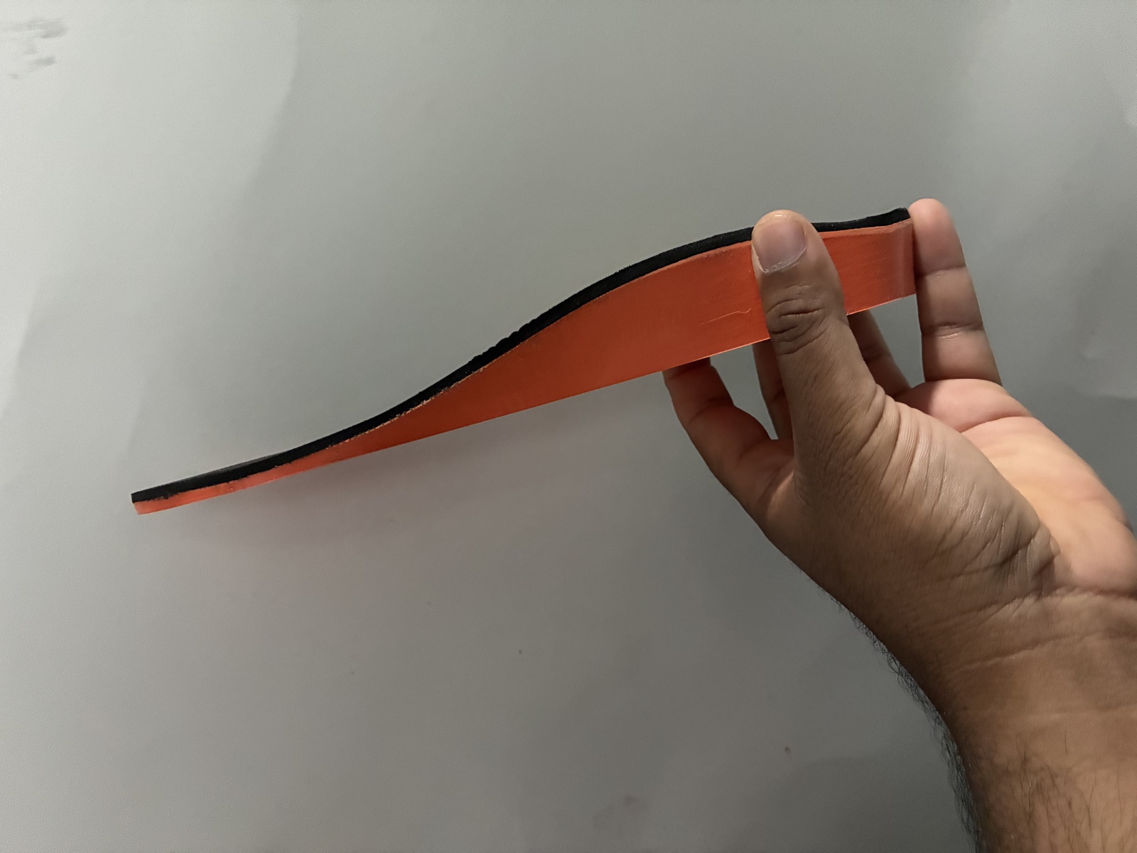 A user holding a finished orange and black orthotic to show its flexibility and arch profile
