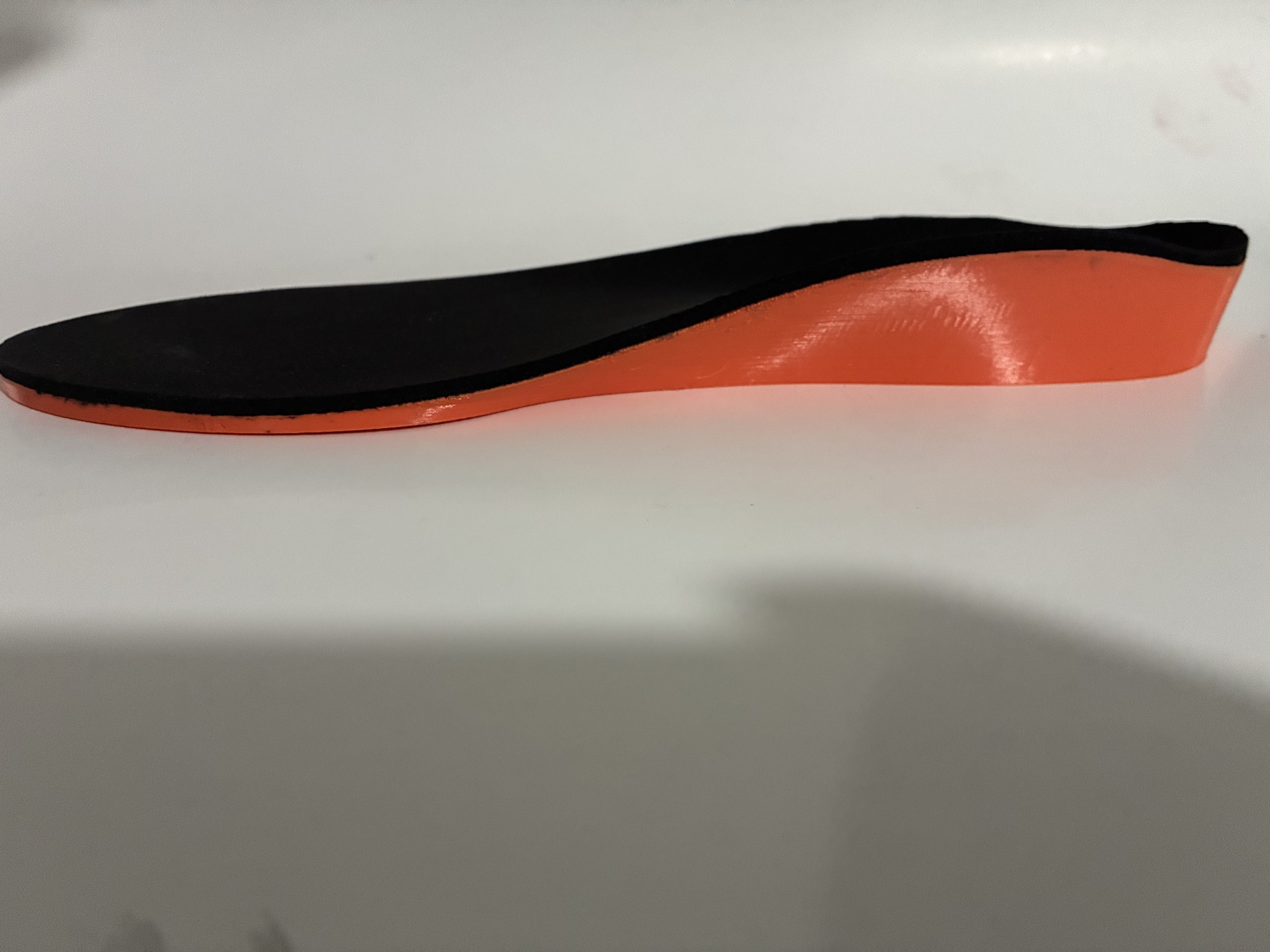 Side profile of an orange 3D-printed orthotic shell finished with a black full-length top cover