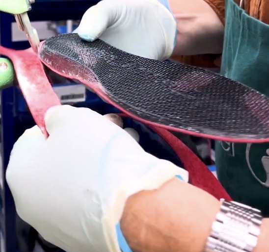 Gloved hands finishing a layered orthotic in a professional workshop