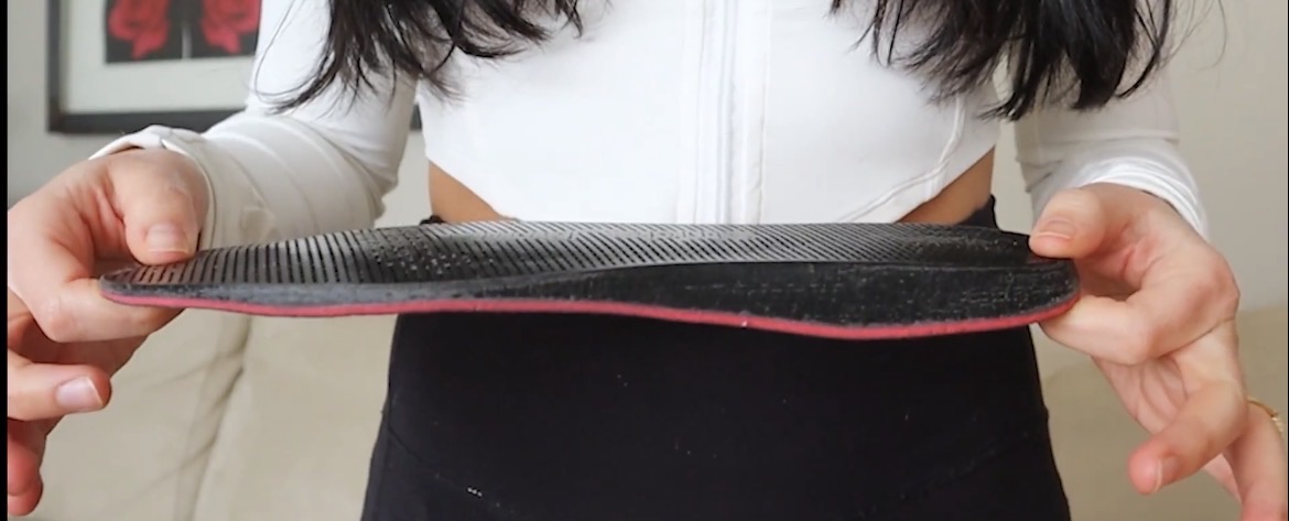 User holding a black lattice insole with a pink full-length layer, showing its side profile